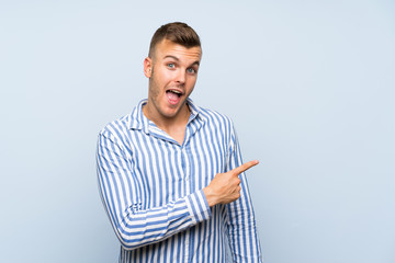 Wall Mural - Young handsome blonde man over isolated blue background surprised and pointing side