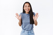 Smiling cute asian girl feeling awkward to refuse friend, raising hands up in surrender or rejection, grinning as saying sorry not gonna come, denying or disapproving something, white background
