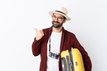 Traveler man man with beard holding a suitcase over isolated white background with thumbs up gesture and smiling