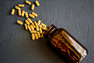 Yellow pills scattered on a black surface near a glass overturned