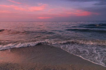 Wall Mural - Coast at sunset. View of surf wave Is covering a sea beach sand. Greece. The Mediterranean Sea. Concept of nature background.