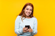 © luismolinero - Teenager redhead girl over isolated yellow background sending a message with the mobile