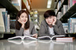 Portrait happy male and female student reading a book in the library