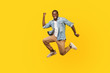 © khosrork - Full length portrait of joyous ecstatic man in denim shirt jumping for joy or flying with raised hand, gesturing yes i did it, celebrating success. indoor studio shot isolated on yellow background