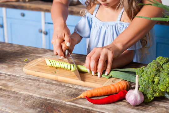 closeup of mother and child chopping vegetable with knife on board, cooking healthy breakfast togeth