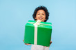 © khosrork - Take this present! Happy generous good-natured little boy with curly hair giving gift box and looking at camera with toothy smile, holiday charity. indoor studio shot isolated on blue background