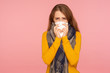 Flu season. Portrait of sick red hair girl wearing big scarf, sneezing and blowing nose, wiping with tissue, suffering temperature and cough, influenza. indoor studio shot isolated on pink background