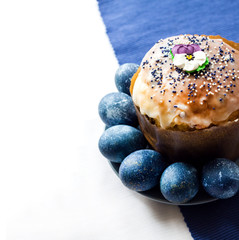 Wall Mural - Easter cake decorated with sugar flower and blue colored eggs on a plate on white and blue cloth background