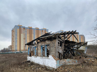 Old ruined house on the background of a new high-rise building. Abandoned house with no doors and windows with a broken roof. Concept: devastation, construction