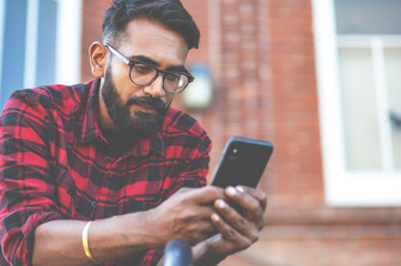 Handsome young man, outdoor. Indian man is texting a message on a cell phone.