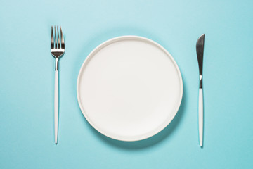 table setting with white plate and cutlery on blue.