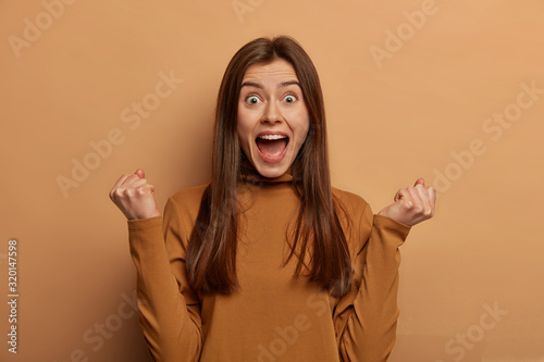 Cuadros en Lienzo Portrait of emotive cheering woman with European appearance, clenches fists, fin