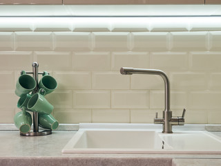 Kitchen faucet and stand with green mugs cups on the background of a white tiled wall in the kitchen