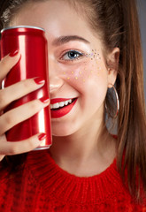 Portrait of beautiful smiling teenager girl in casual hipster clothes with stylish trendy makeup white drinking cool soda cola drink from red can in hand. Smiling face with beautifil eyes and red.