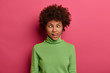 © wayhome.studio  - Curly haired female crosses eyes and sticks out tongue, feels like crazy clown, wears green turtleneck, makes grimace, foolishes around, stands against pink background, shows hilarious funny face