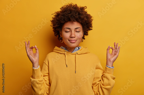 Fotomural Portrait of ethnic woman stays calm, meditates and practices yoga, keeps hands i