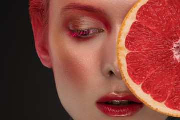 portrait of a girl with red make-up and grapefruit looking at the camera