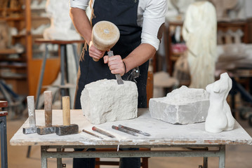 bearded craftsman works in white stone carving with a chisel. creative workshop with works of art.