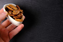 Hand Is Holding A White Plate Filled With Brown Pecans On A Gloomy Background