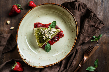 Wall Mural - Matcha green tea cake with creamy filling, nuts, strawberry jam and mint on plate over wooden background. Delicious sweets and dessert, top view