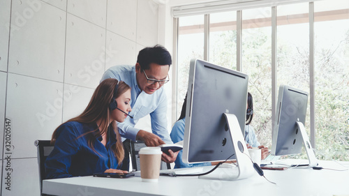Fotomural Customer support agent or call center with headset works on desktop computer while supporting the customer on phone call