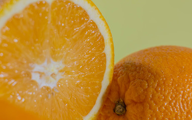 Halved orange near a whole orange on a green background