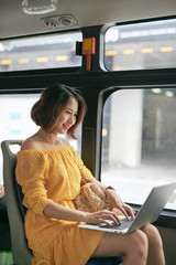 Wall Mural - Young businesswoman on a business travel. Working on the bus using her laptop.