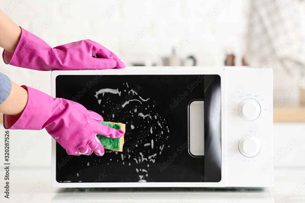 Woman cleaning microwave oven in kitchen