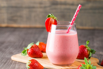 Glass of fresh strawberry milkshake, smoothie and fresh strawberries on pink, white and wooden background. Healthy food and drink concept.