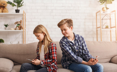 Wall Mural - Curious Brother Reading Sister's Messages On Phone Sitting On Couch