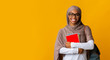 Smiling afro muslim female student in headscarf and eyeglasses holding notebooks