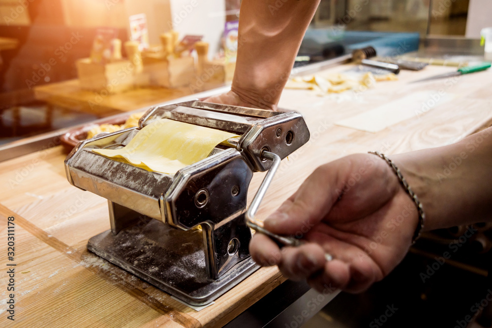 Chef rolling dough with a pasta machine. Pasta maker machine.  - obrazy, fototapety, plakaty 