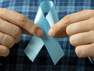 A man in a plaid shirt holds two hands blue Ribbon symbol of prostate cancer awareness.Concept of medicine and mans health care