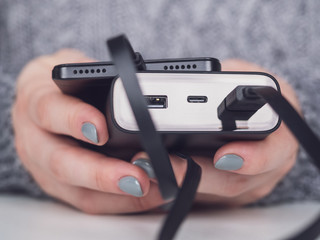 Power bank charges the phone in women's hands. The girl holds a smartphone and an external battery. Close-up of a portable power bank . USB and usb type-c connectors