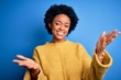 Young beautiful African American afro woman with curly hair wearing yellow casual sweater smiling cheerful offering hands giving assistance and acceptance.