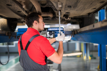 Wall Mural - Car man mechanic examining car suspension of lifted automobile at repair service station