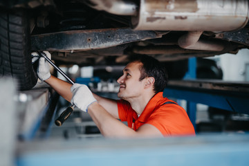 Wall Mural - Car man mechanic with spanner tighten car suspension detail of lifted automobile at repair service station