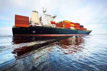 Wall Mural - Large cargo container ship leaving the port of Norfolk, close-up. Cloudy blue sky. Virginia, USA