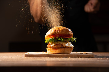 Make it pro, home made hamburger made by white sesame bun, tomato slice, salad, cheese, grilled meat and onion on wooden tray wooden table with cooking decorate chef hand in dark isolate background