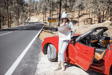 Wall Mural - Woman enjoying road trip, standing with map near convertible car on the roadside in the volcanic mountain forest on Tenerife island, Spain