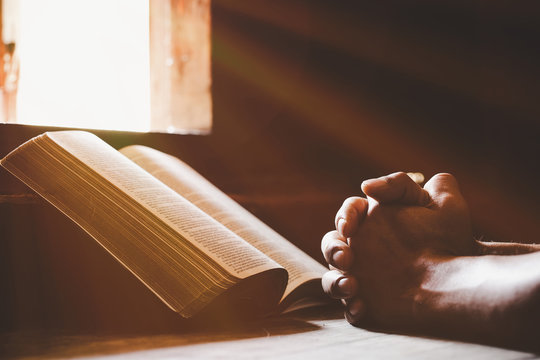 Soft focus on a hand of man while praying for christian religion with blurred of dark background.