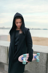 Portrait of a skater style teenager girl in black hood-jacket with pink skateboard