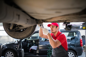 Wall Mural - Car mechanic with spanner tighten car suspension detail of lifted automobile at repair service station