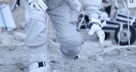 nasa astronaut walking the moon or uninhabited planet, leaning and taking piece of soil in hand to d