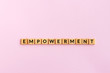 Empowerment text wood blocks. Pink background.