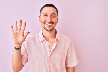 Poster - Young handsome man wearing pink shirt standing over isolated background showing and pointing up with fingers number five while smiling confident and happy.