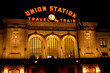 Union Station in Denver, Colorado at night as the sign is illuminated in orange and pierces the dark sky. 
