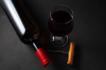 Wall Mural - a glass of grape wine next to a sealed bottle of wine on a dark table