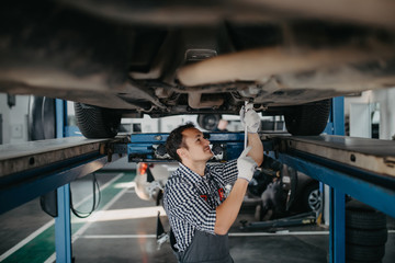 Wall Mural - Car mechanic with spanner tighten car suspension detail of lifted automobile at repair service station