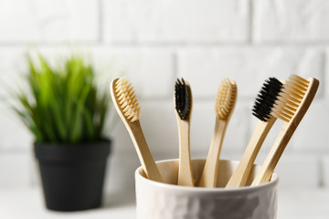 Close up of several biodegradable bamboo toothbrushes in a white glass on a brick wall background. Image with copy space, horizontal orientation. Zero waste concept.